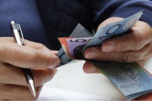 hands of a senior woman holding australian banknotes and a pen